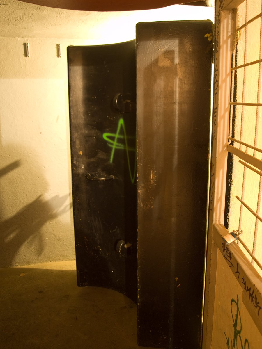 Ciężkie, hermetyczne drzwi schronu (blast door). Schron to budowla ochrony zbiorowej z filtrowentylacją, chroniąca przed falą uderzeniową i skażeniami. · źródło: Honza Groh, Wikimedia Commons, CC BY-SA 3.0