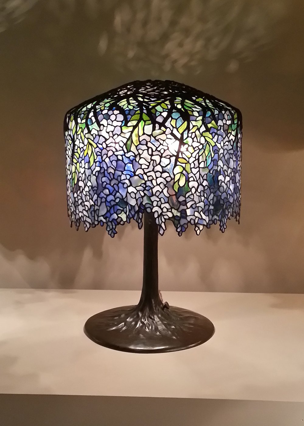 Louis Comfort Tiffany, lampa witrażowa Wisteria (Tiffany Studios) — kopuła z kawałków kolorowego szkła spojonych folią miedzianą: kwitnąca glicynia jako secesyjny przedmiot luksusowy · źródło: fot. Fopseh, Wikimedia Commons, CC BY-SA 4.0